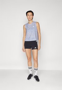 Ærmeløs lyseblå sportstop med et struktureret mønster, parret med sorte shorts med hvide striber og logo. Sorte sportssko og sokker.