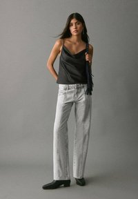 Črna satenska majica s tankimi naramnicami, kombinirana z visoko pasom, svetlo sivo širokimi hlačami in črnimi čevlji z visoko peto.