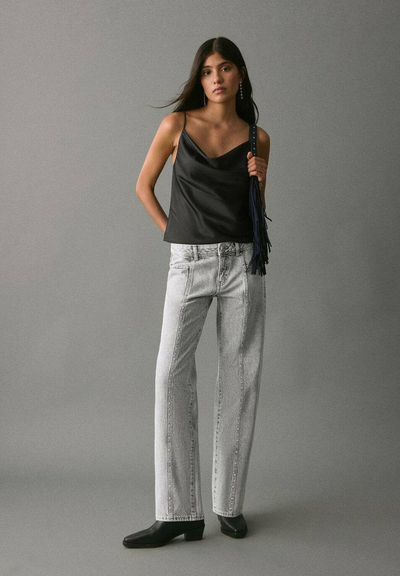 Črna satenska majica s tankimi naramnicami, kombinirana z visoko pasom, svetlo sivo širokimi hlačami in črnimi čevlji z visoko peto.