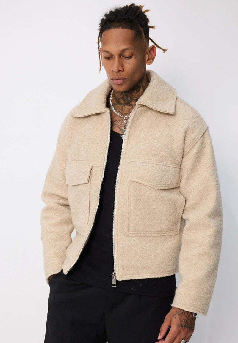 Veste en polaire beige avec col, deux poches avant et une fermeture éclair frontale. Le tissu a une texture douce et un aspect légèrement duveteux.