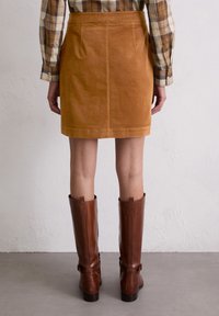Bruine corduroy rok met een rechte snit en zichtbare stiksels, gecombineerd met hoge bruine leren laarzen met gespservers.