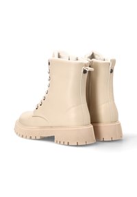 Botas de tobillo de cuero beige con suela de goma texturizada, cordones en la parte delantera y cremallera lateral. Forro suave visible en la parte superior.