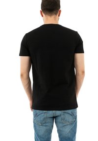 Camiseta negra de manga corta con cuello redondo, hecha de algodón. Llevada con jeans de mezclilla azul claro que presentan detalles cosidos en los bolsillos traseros.