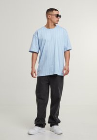 Light blue oversized t-shirt with white vertical stripes, paired with black baggy pants and white sneakers. Accessories include dark sunglasses.