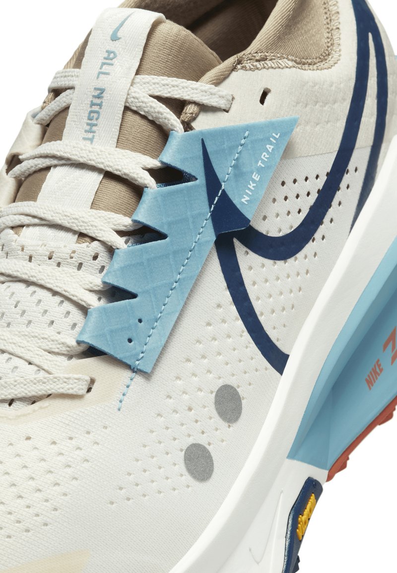 Scarpa sportiva beige chiaro con tomaia in mesh traspirante, dettagli blu, perforazioni per la ventilazione e suola bianca ammortizzata.