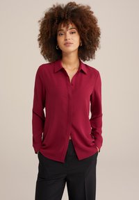 Burgundy långärmad skjorta med knappstängning framtill, krage och en avslappnad passform, tillverkad av lätt tyg med en subtil struktur.