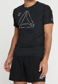 Black athletic t-shirt with a textured finish, featuring a white geometric logo on the front and short sleeves. Paired with black shorts.