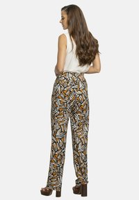 Pantalones de talle alto y corte holgado con un atrevido patrón abstracto en negro, blanco y naranja. Fabricados en una tela ligera. Tacones gruesos.
