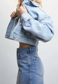 Giacca cropped in denim azzurro chiaro con chiusura a bottoni e maniche oversize, abbinata a una gonna in denim a vita alta dello stesso colore.