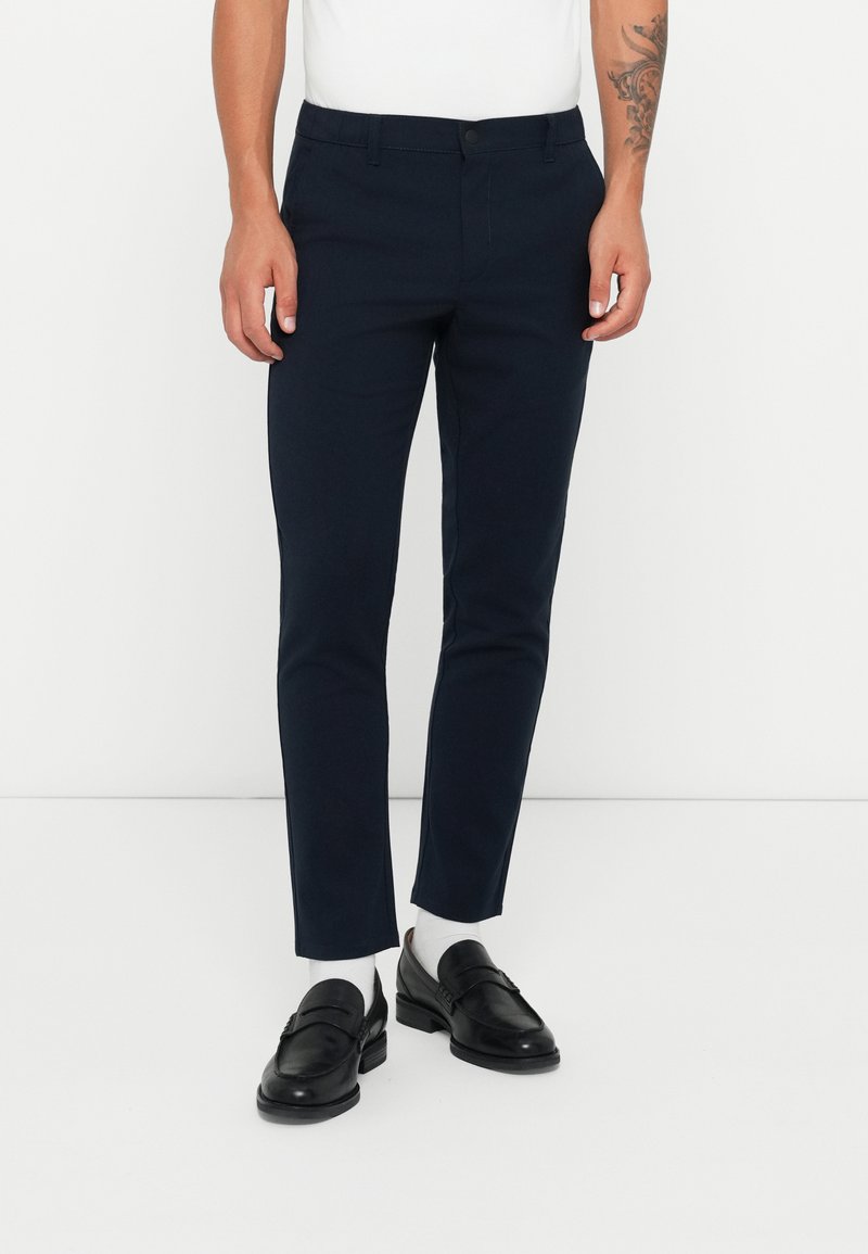 Marineblaue maßgeschneiderte Hose mit slim Fit, gefertigt aus glattem Stoff, mit Knopfverschluss, Taschen und dezentem Steppdetail.