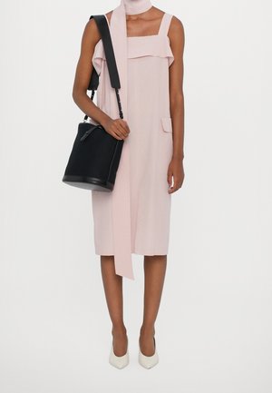 Lyserød ærmeløs kjole med flæsekant ved halsen, to sidelommer, kombineret med en sort bucket taske og hvide spidse hæle.