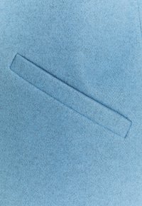 Ljusblå filt med en slät yta, med en horisontell fickdetalj som är sydd på ytan.