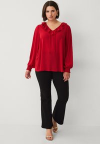 Rode blouse met lange mouwen, een gerimpelde halslijn en een koordje. Gecombineerd met zwarte flared pantalons en metallic gouden sandalen.