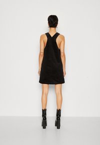 Svart manchesterklänning med ärmlös design och ett korsryggsdetalj. Tyget har en texturerad yta och slutar ovanför knät.