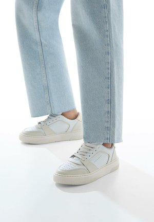 Witte casual sneakers van textuurleer met geperforeerde teen. Dikke rubberen zool. Gepaard met lichtblauwe wijde spijkerbroek.