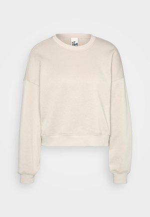 Beżowy sweter z okrągłym dekoltem, krótszy fason, z długimi rękawami oraz ściągaczami u dołu i przy mankietach, eksponowany na jasnoszarym tle.
