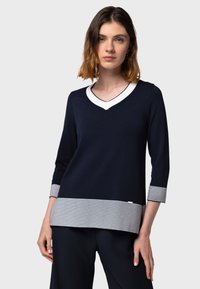 Top navy a scollo a V con maniche tre quarti, caratterizzato da un bordo bianco al colletto e dettaglio a righe sull'orlo. Tessuto a maglia morbido con vestibilità comoda.