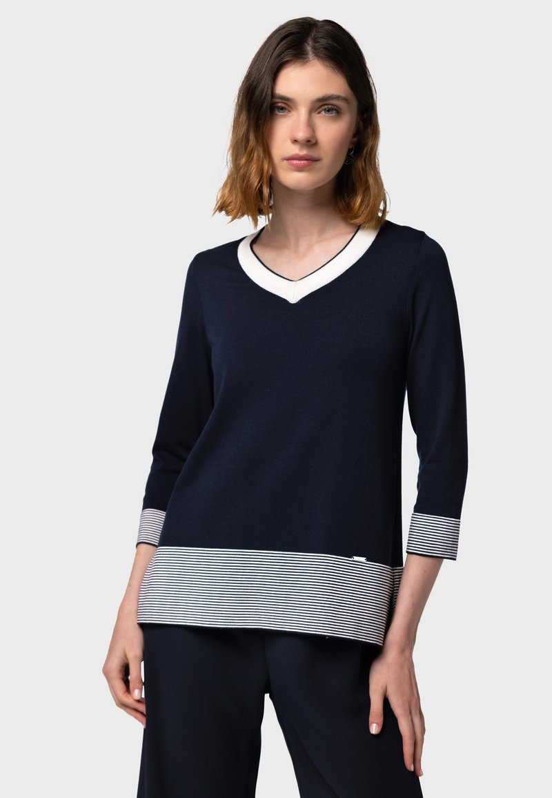 Top navy a scollo a V con maniche tre quarti, caratterizzato da un bordo bianco al colletto e dettaglio a righe sull'orlo. Tessuto a maglia morbido con vestibilità comoda.
