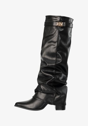 Bota negra de cuero holgada hasta media pantorrilla, con punta puntiaguda, tacón ancho y una correa decorativa con hebilla dorada cerca de la parte superior.