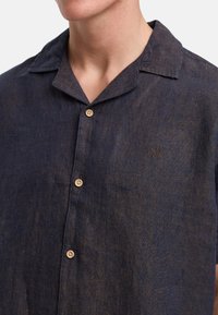Camisa de lino de manga corta en azul oscuro con cuello, que cuenta con un cierre de botones y un pequeño logo bordado en el pecho.