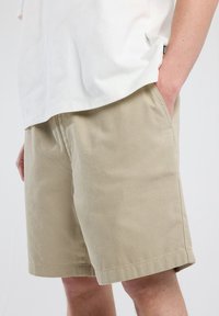 Shorts de algodón beige con bolsillos laterales, corte regular y dobladillo cosido. Llevado con una camiseta blanca de corte holgado.