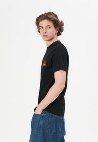 Sort kortærmet t-shirt med et farverigt grafisk design på fronten, parret med blå denim jeans.
