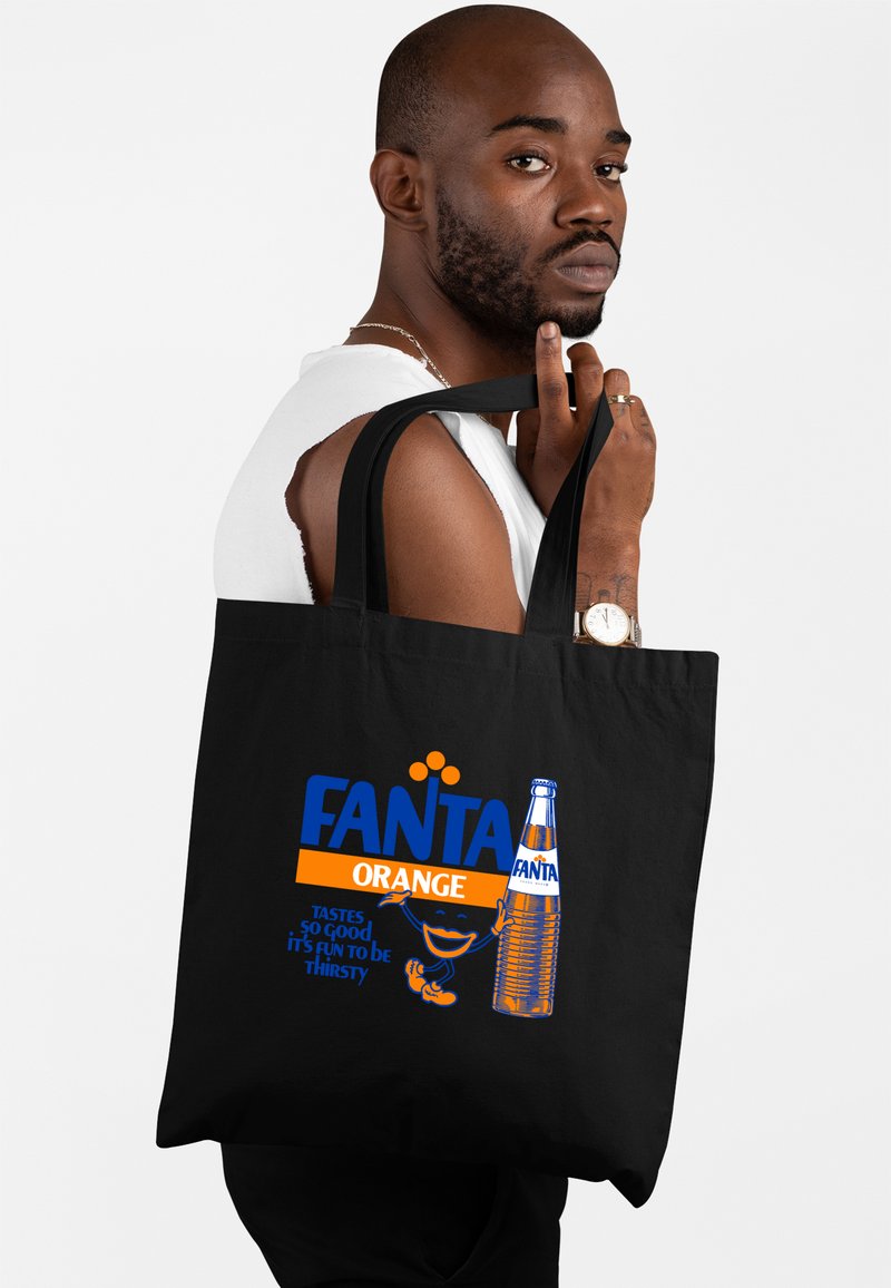 La borsa tote nera in tela presenta un vivace branding Fanta in blu e arancione. Il design include un'illustrazione di una bottiglia Fanta in stile retro e del testo.