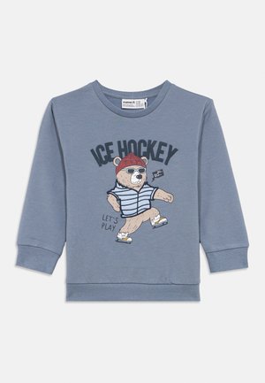Világoskék pulóver kerek nyakkal és hosszú ujjakkal. Jellemzője egy medve grafika csíkos ruhában, rajta az "ICE HOCKEY" felirattal.