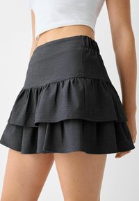 Musta röyhelöinen minihame, jossa on teksturoitu kangas, joustava vyötärö ja kolme vaakasuoraa röyhelökerrosta.