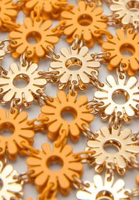 Plastic en metalen bloemvormige bedels in oranje en goud die met elkaar verbonden zijn, met uitsparingen in het midden en verhoogde bloemblaadjes ontwerpen.