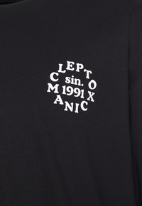 Schwarzes Baumwoll-T-Shirt mit einem weißen, kreisförmigen grafischen Textdesign, auf dem die Worte "LEPTO C sin. 1991 X MANIC" in unterschiedlichen typografischen Stilen zu sehen sind.