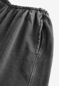 Grå joggebukser med elastisk talje, der har en diskret ribbet tekstur og sidelommer. Materialet ser blødt og let ud.
