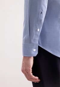 Camicia da uomo azzurro chiaro con motivo, realizzata in un tessuto intrecciato testurizzato. Presenta polsini con bottoni bianchi e un colletto a contrasto.