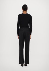 Haut noir à manches longues, avec un petit logo à l'arrière, associé à un pantalon à rayures fines gris foncé. Tissu lisse avec une coupe ajustée.