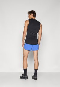 Schwarzes ärmelloses Top, blaue Shorts mit einem leichten Glanz, schwarze Sportschuhe und Socken. Einfaches, körpernahes Design ohne sichtbare Logos oder Muster.