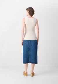 Top beige a righe senza maniche abbinato a una lunga gonna in denim blu. L'outfit è completato da scarpe marroni slip-on con una finitura testurizzata.