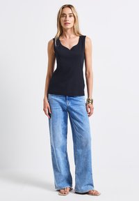 Top senza maniche blu marina con scollatura a V abbinato a jeans a gamba larga di un blu chiaro. Il tessuto è liscio e ha una consistenza morbida.