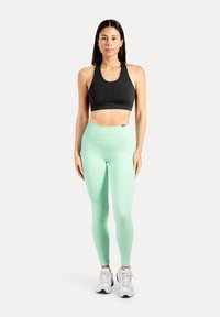 Svart sport-bh med rundad halsringning tillsammans med mintgröna högmidjade träningsleggings, båda gjorda av stretchigt material. Vita träningsskor.