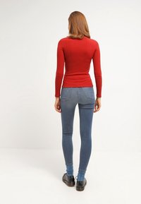 Top lungo a maniche lunghe rosso a costine, abbinato a jeans skinny blu chiaro. I jeans presentano un classico design a cinque tasche e una vestibilità alla caviglia.