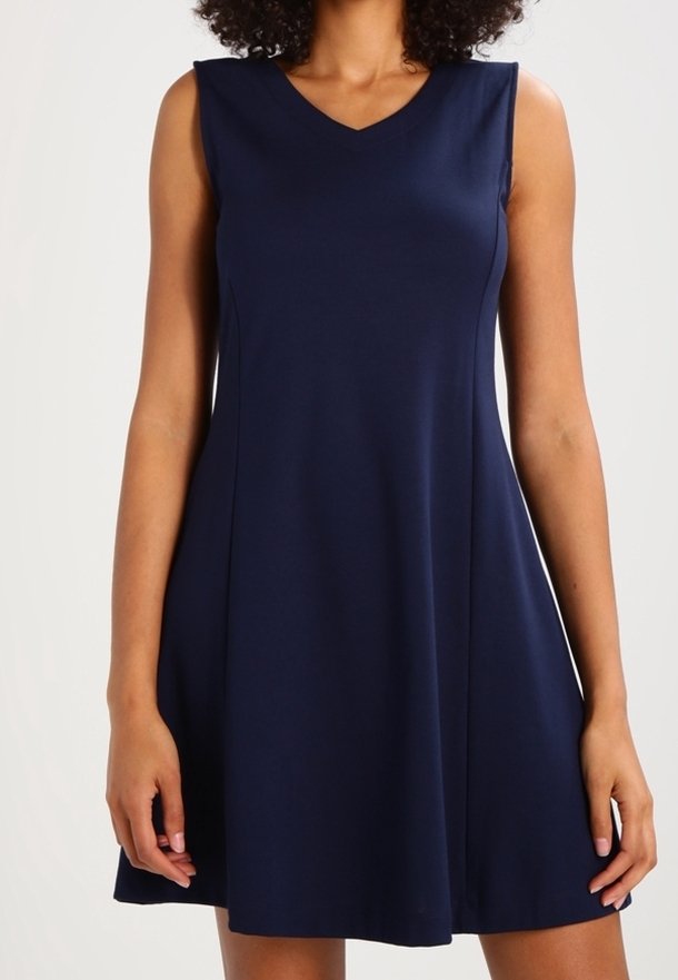 Robe trapèze bleu marine sans manches avec un col en V portée par une personne aux cheveux bouclés, montrée des épaules jusqu'à mi-cuisse.