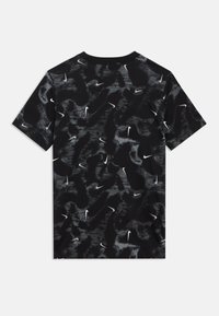 Juoda trumpomis rankovėmis marškinėliai su tekstūriniu, abstrakčiu raštu ir išmėtytais baltos spalvos Nike logotipais. Pagaminti iš minkšto, orui pralaidaus audinio.