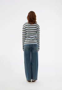 Chemise à manches longues rayée en vert et bleu, associée à un jean bleu à jambes larges. La chemise présente des rayures horizontales ; le jean possède des poches arrière.