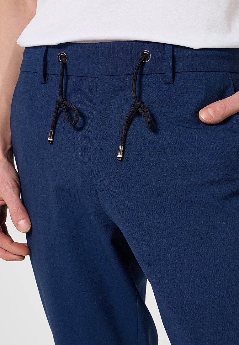 Granatowe spodnie o gładkiej fakturze, elastycznym pasku z sznurkiem i subtelnymi bocznymi kieszeniami. Wykończenia obejmują srebrne akcenty.