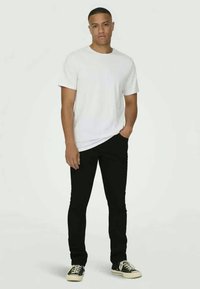 Tricou alb din bumbac, asortat cu blugi negri slim-fit. Persoana poartă adidași negri și albi. Design simplu, curat, fără modele.