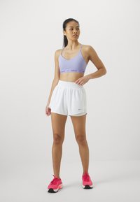 Lilás sportmelltartó Nike logóval, fehér elasztikus derekú rövidnadrág és rózsaszín futócipő fekete részletekkel. Egyszerű, sportos dizájn.
