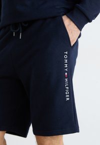 Granatowe szorty wykonane z miękkiego materiału, z elastycznym paskiem oraz sznurkiem do regulacji. Na lewej stronie znajduje się biały logo "TOMMY HILFIGER".