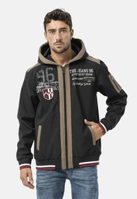 Zwarte jas met ritssluiting, grijze en bruine accenten, voorzien van capuchon, voorzakken en logoprints. Gestructureerde stof met geribbelde manchetten.