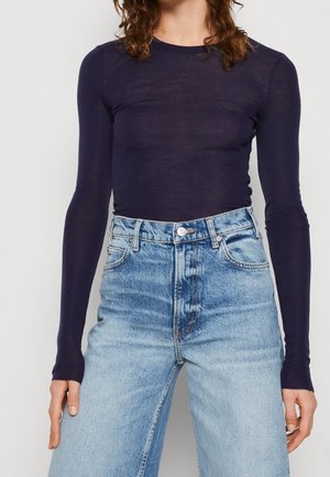 Personne portant un haut ajusté à manches longues violet foncé rentré dans un jean large taille haute bleu clair.