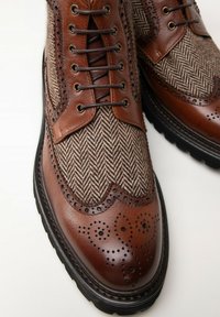 Hnědé kožené boty s textilním svrchním dílem ve vzoru herringbone, zdobené perforovanými brogue vzory a kontrastní černou gumovou podrážkou.