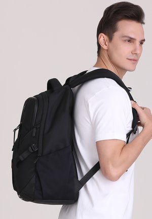 Sac à dos noir au design épuré, avec plusieurs compartiments zippés, des bretelles rembourrées et une texture en maille sur le panneau arrière.